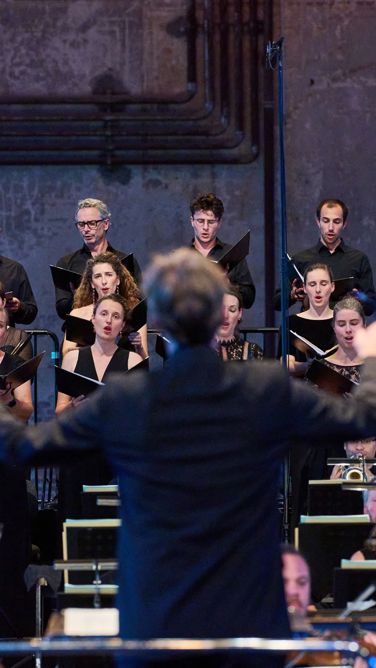 Concert photo with the singers of Chorwerk Ruhr, with conductor Florian Helgath blurred in the foreground.
