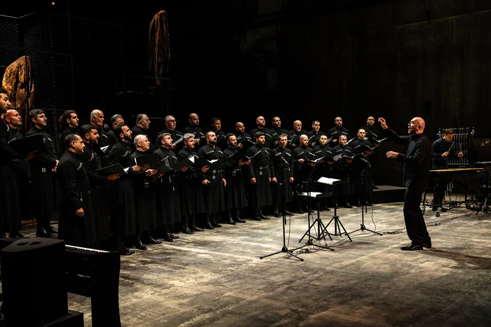 Ein Männerchor singt in einer Halle, vor ihnen steht der Dirigent.