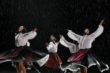 Scene from Balkan Erotic Epic: Performers in traditional clothing dance in the rain and raise their arms to the sky.
