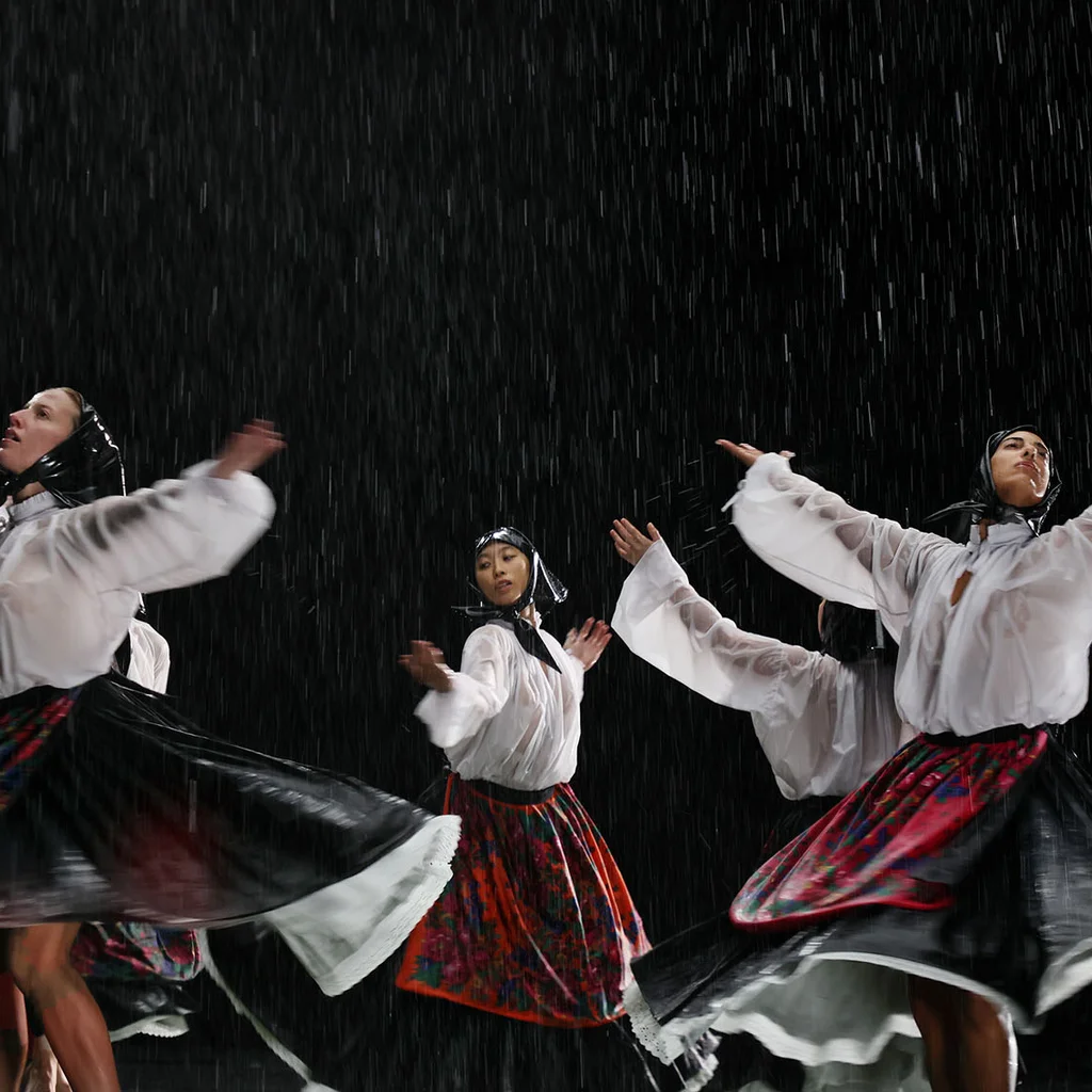 Scene from Balkan Erotic Epic: Performers in traditional clothing dance in the rain and raise their arms to the sky.