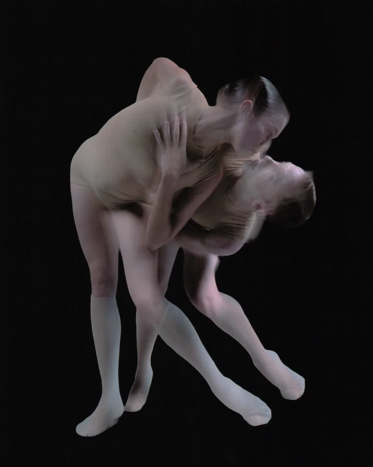 Two dancers in skin-toned costumes bend closely toward each other. The depiction creates a sense of intimacy, suspension, and temporal overlap.