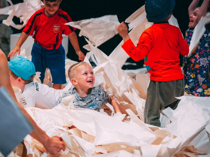 Kinder spielen fröhlich mit großen Papierbögen.