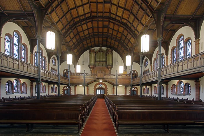 The interior of the Protestant church on Katernberger Markt features a high wooden ceiling with dark beams, large arched stained-glass windows, and an imposing organ on the gallery above the entrance.