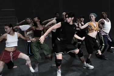 Several people perform a choreographed movement together on a rehearsal stage.