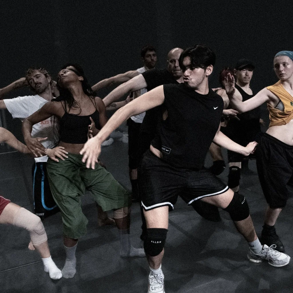 Mehrere Personen bewegen sich gemeinsam in einer choreografierten Szene auf einer Probebühne.