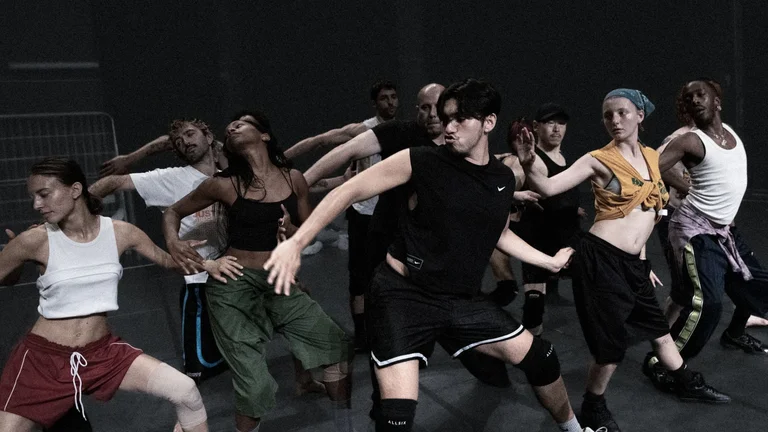 Mehrere Personen bewegen sich gemeinsam in einer choreografierten Szene auf einer Probebühne.