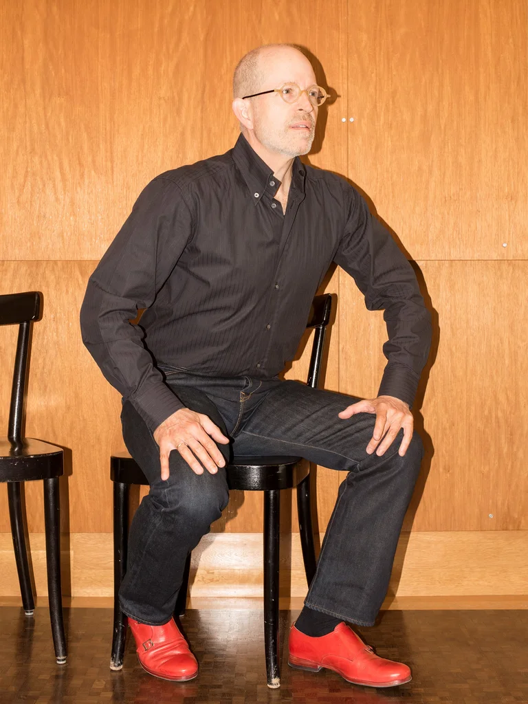 Man with red shoes, sitting on a chair in front of a wooden wall