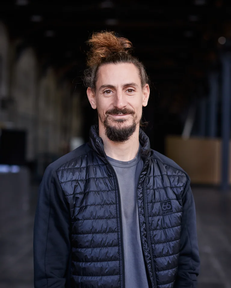 Ein Mann mit Zopf, der Choreograf Ioannis Mandafounis, lächelt in die Kamera.