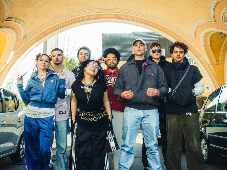 Group picture of Patina Records, posing together between two cars under an bright arched driveway.