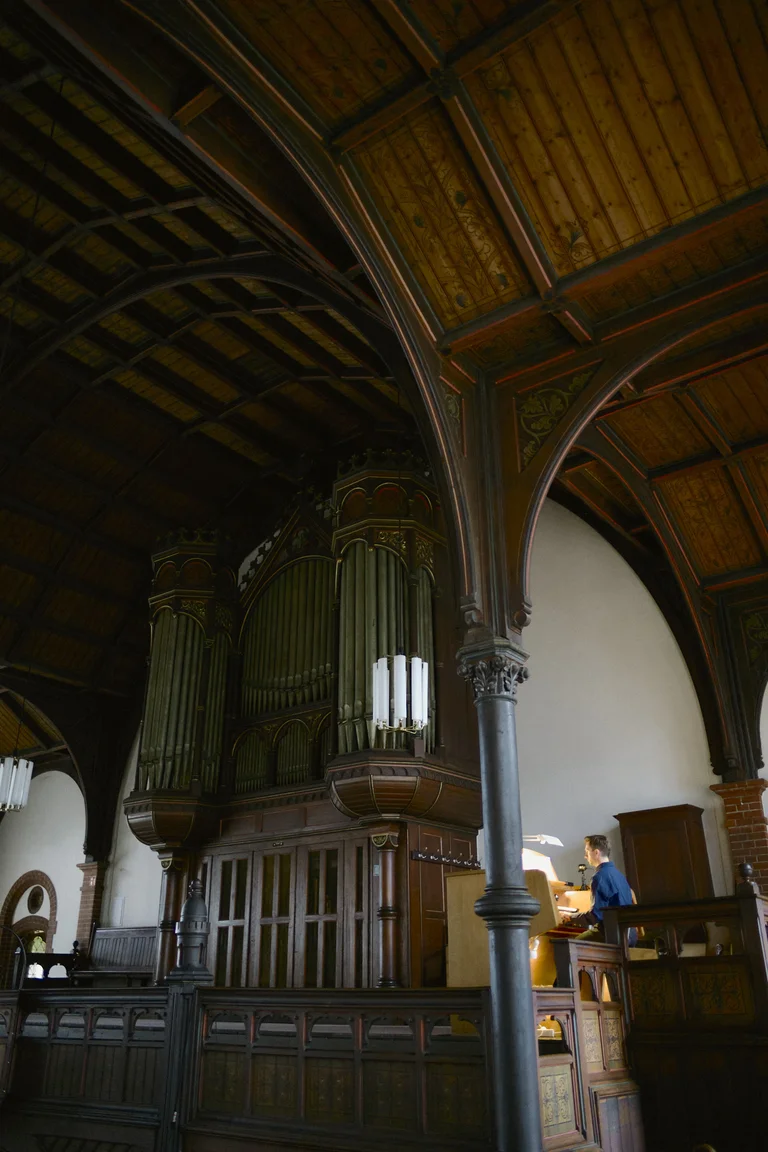 Organist James McVinnie performing at the grand organ of the Evangelical Church at the Market in Katernberg during the event 124 Years of Reverb. He is seated at the console on the gallery, with the monumental organ pipes and ornate wooden architecture of the church visible in the background.