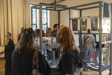 Besucher:innen betrachten Fotografien und Objekte in einer Ausstellung.