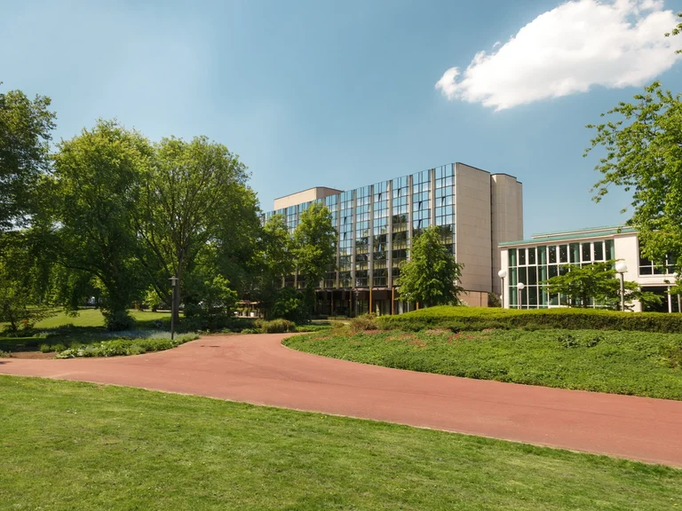 Exterior view of the Sheraton Hotel in Essen, surrounded by green parkland on a sunny day.