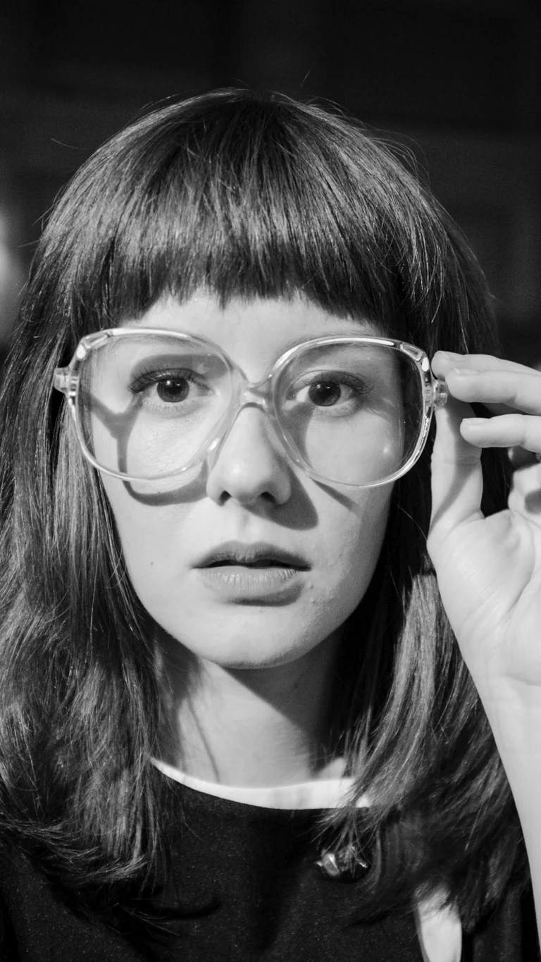 Schwarz-weiß Film still aus dem Film "Leto", das eine Person in Nahaufnahme zeigt, die sich an die Brille fasst.