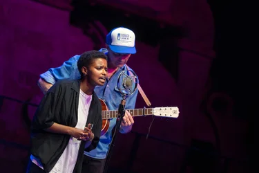 Meskerem Mees singt am Mikrofon, begleitet von dem Gitarristen Carlos Garbin auf einer dunkel beleuchteten Bühne.
