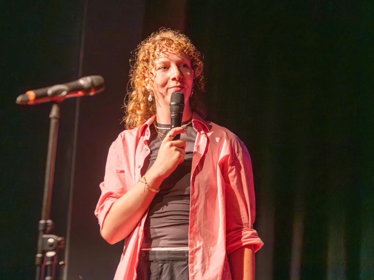 Jana Goller stands on stage holding a microphone and smiling at the audience.
