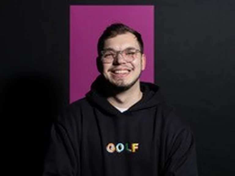 Portrait von Tobias Pappert, der lächelnd und mit verschränkten Armen vor pinkem Hintergrund steht.