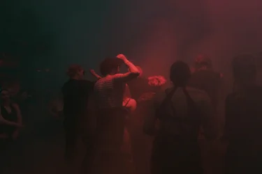 Eine Gruppe tanzt in rotem Licht, teils im Nebel verschwommen.
