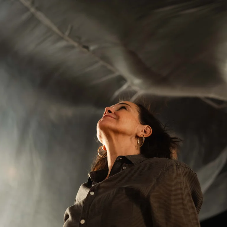 A person looks upward on a stage as a large translucent sheet billows overhead.