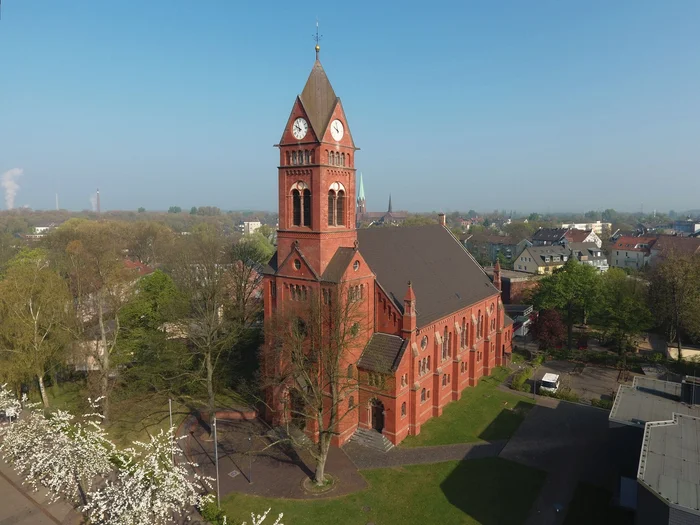 The Protestant church on Katernberger Markt from a bird’s-eye view, surrounded by a green urban district with residential buildings, trees, and industrial chimneys in the distance.