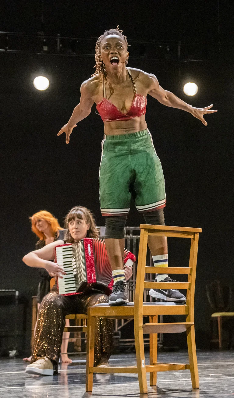 Stage actor in a chair, in the background further actors with music instruments