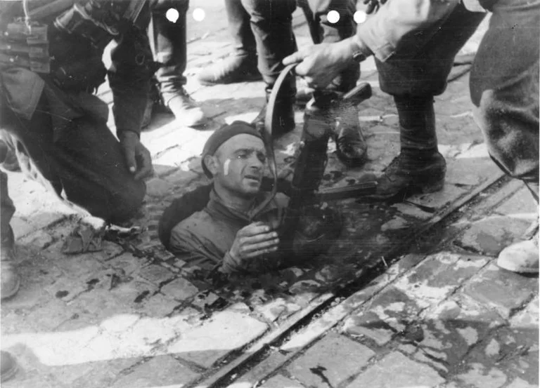 Home Army soldier from the Mokotów District surrenders to German troops. He's pulled up from a hole in the street.