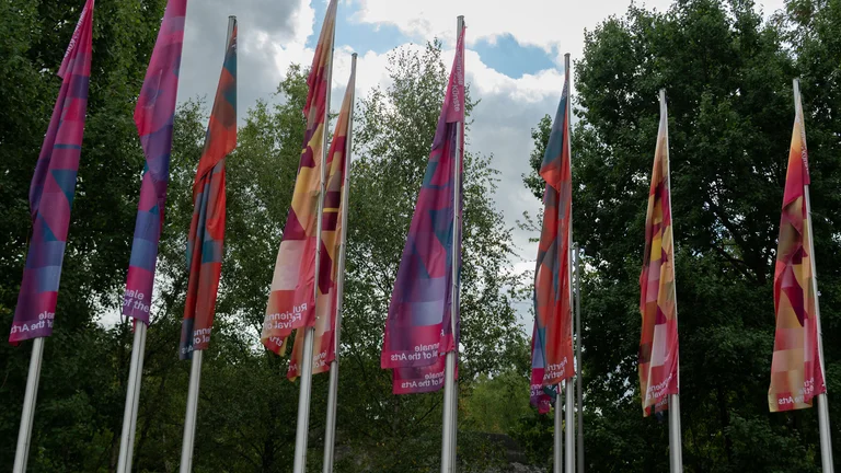 Bunte Fahnen der Ruhrtriennale an Fahnenmasten angebracht und nebeneinander stehend.