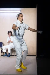 Israel Galván bewegt sich im Vordergrund mit ausgestreckten Armen; im Hintergrund sitzt Marlene Monteiro Freitas auf einem Stuhl.