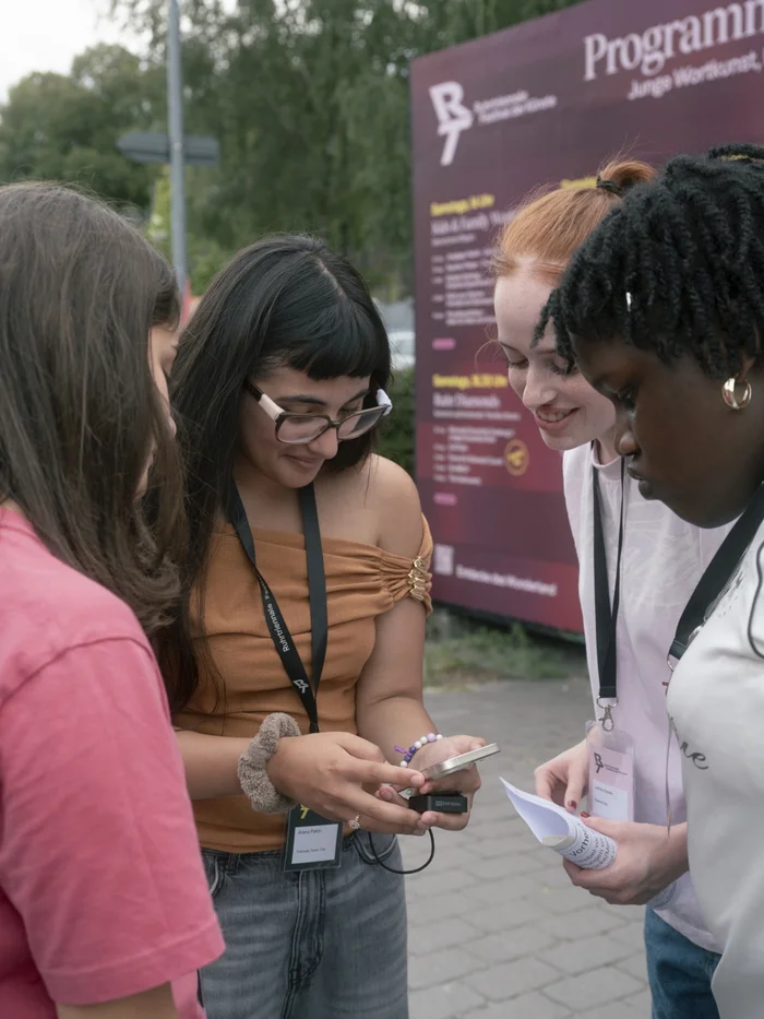 Four young women stand together at the festival centre, looking at a recording device and their notes.