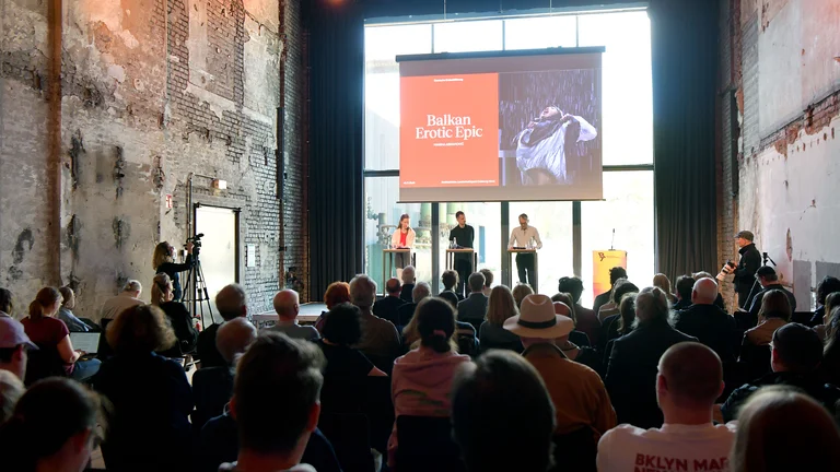 Aufnahme der Programm-Pressekonferenz der Ruhrtriennale 2026 im Dampfgebläsehaus Bochum. Im Vordergrund sitzen Pressevertreter:innen, während im Hintergrund Intendant Ivo Van Hove, Kyrstian Lada und Britta Schünemann unter einem großen Screen stehen.