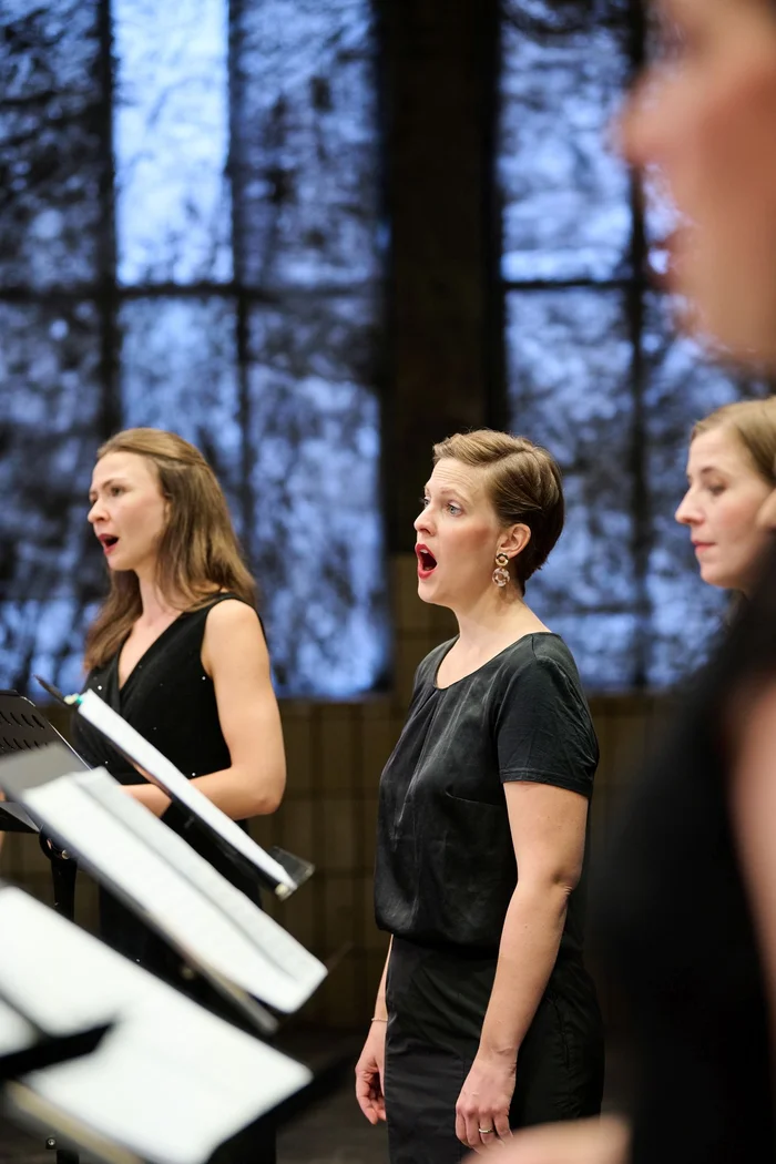 Das Chorwerk Ruhr in der Turbinenhalle in Bochum für die Produktion 'Rechants', die Ruhrtriennale 2024. Der Chor steht vor der Installation von Berlinde De Bruyckere 'City of Refue IV'. Wir sehen den Chor von rechts, eine Frau singt. Noten stehen vor ihr