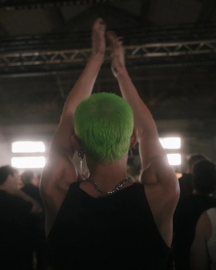 A person with green-dyed hair stands in the crowd, clapping with raised arms.