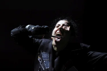 Scene from Balkan Erotic Epic: A person screams with their mouth wide open while holding a knife against their tongue. Strong light-shadow contrasts heighten the dramatic effect.