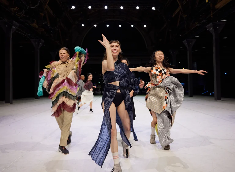 Mehrere Tänzer:innen der Dresden Frankfurt Dance Company stehen in bunten Kostümen auf einer Bühne.um.