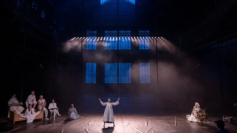 A view into the dark, dimly lit Jahrhunderthalle Bochum. The performers from the 2024 production "Haugtussa"can be seen in the foreground.