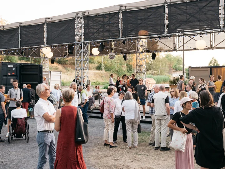 Gruppen von Menschen, die sich bei der Ruhrtriennale unter einer offenen Bühnenkonstruktion unterhalten.