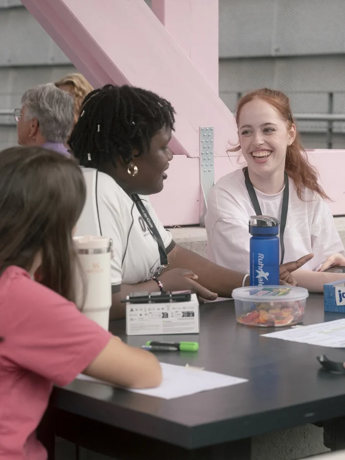 Two young women chat and laugh together at a table in the festival centre.