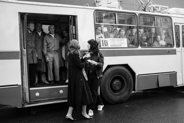 Schwarz-weiß Film still aus dem Film "Leto", auf dem zwei Personen vor einem Passagierbus stehen.