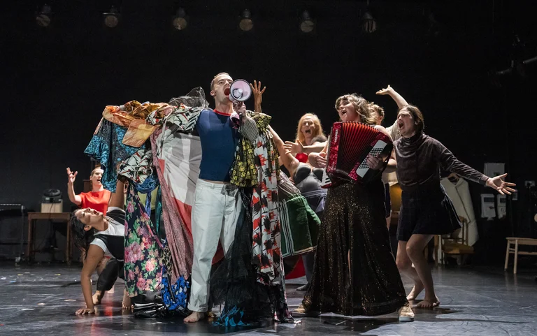 A group of dancers in colorful clothing on a stage with musical instruments and a megaphone