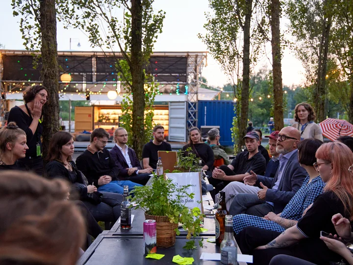 Die Mitglieder des Club.Ruhr im Gespräch mit Beteiligten der Ruhrtriennale in der Pappelwaldkantine, umgeben von Bäumen und Lichterketten.