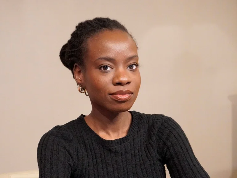A portrait of Orliane Yomi, who is resting her arms on a table in front of her and looking into the camera.