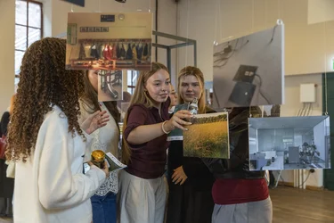 Gruppe junger Frauen betrachtet gemeinsam aufgehängte Fotografien in einer Ausstellung.