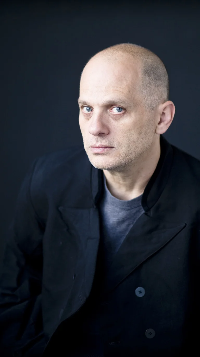 Der Komponist David Lang trägt dunkle Kleidung und schaut vor einem schwarzen Hintergrund ernst in die Kamera. Auf dem Portraitfoto ist er nur vom Oberkörper aufwärts zu sehen.