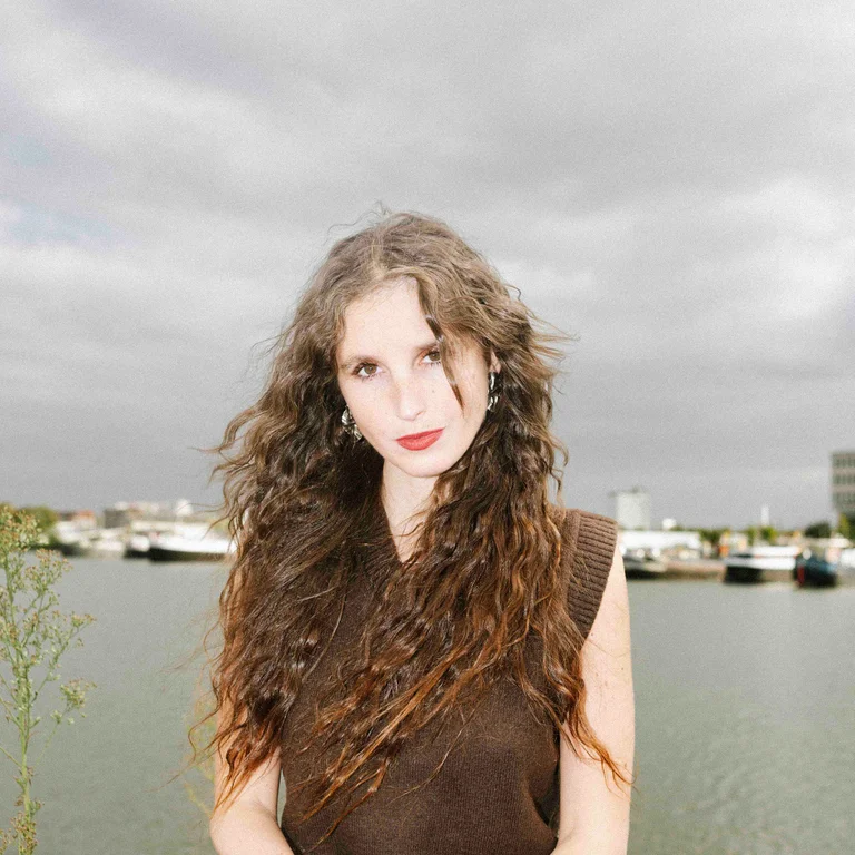 Portrait of Lisaboa Houbrechts sitting at a river and looking into the camera.