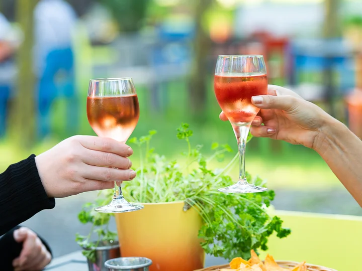 Two hands clinking filled wine glasses.